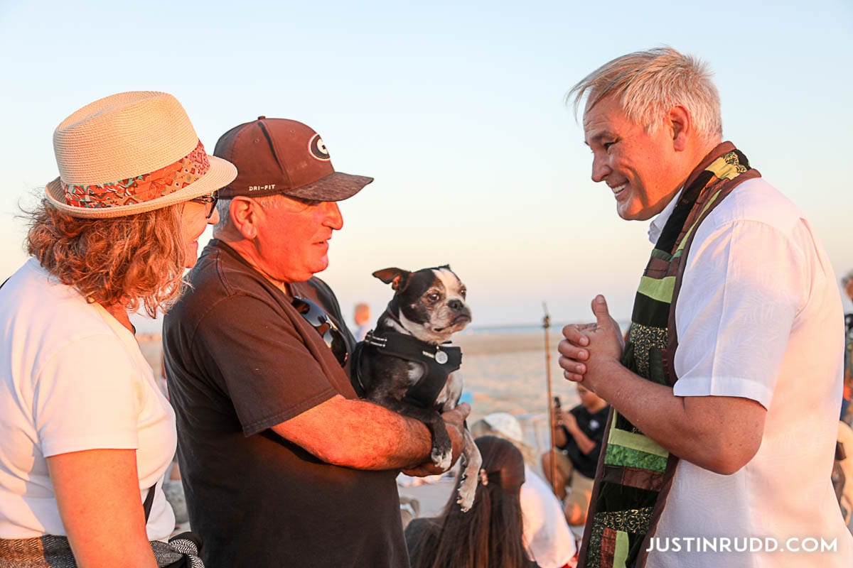 A man stands between another man and woman while holding up a black and white dog.