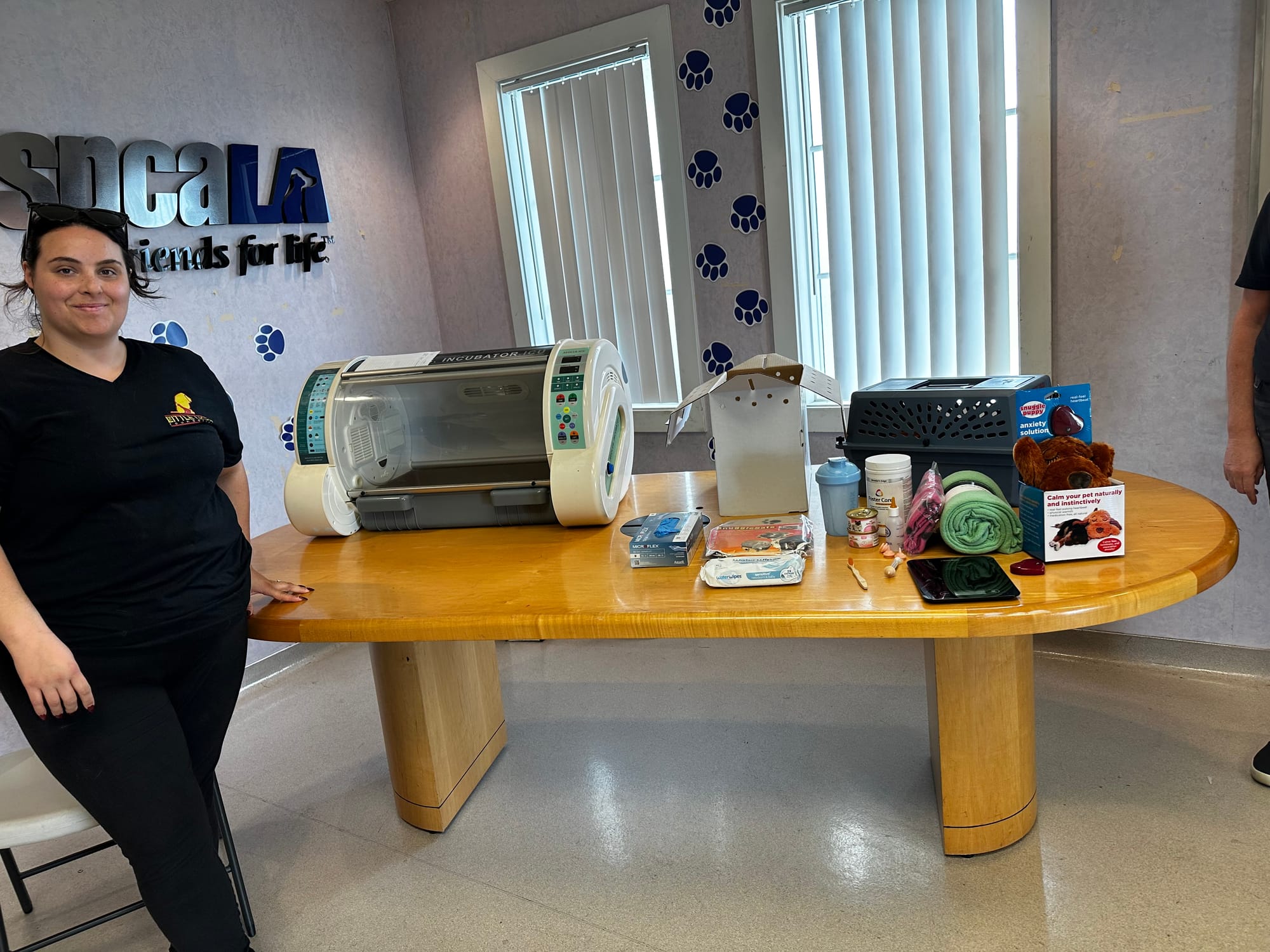 A woman stands next to a table covered in assorted items.
