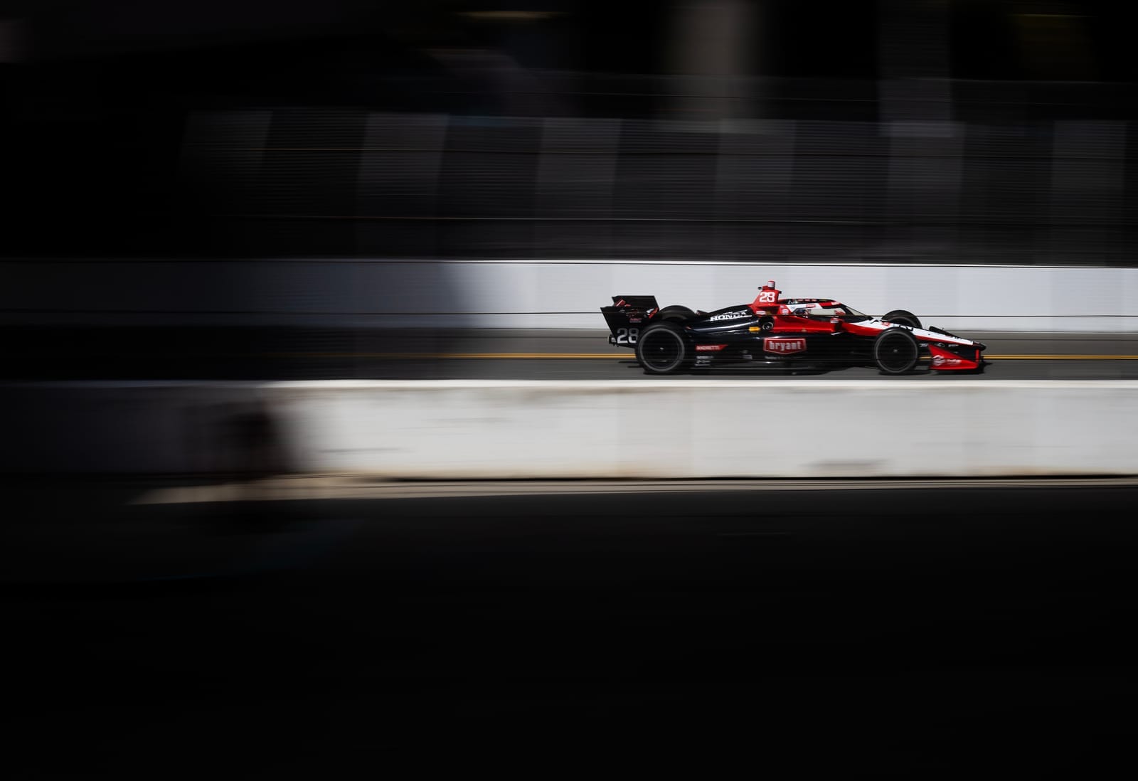 A red race car drives fast between two concrete barriers.