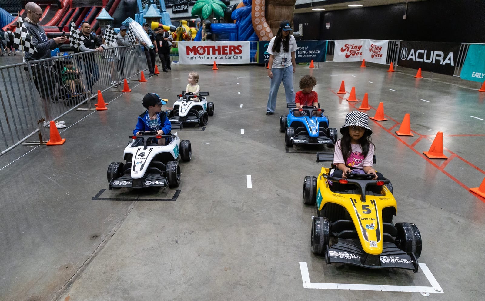 Four children sit in colorful go-karts at the start of a race.