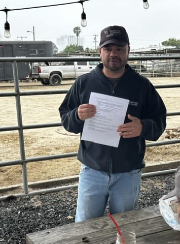 A man stands outside near a metal fence holding a piece of paper with writing on it.