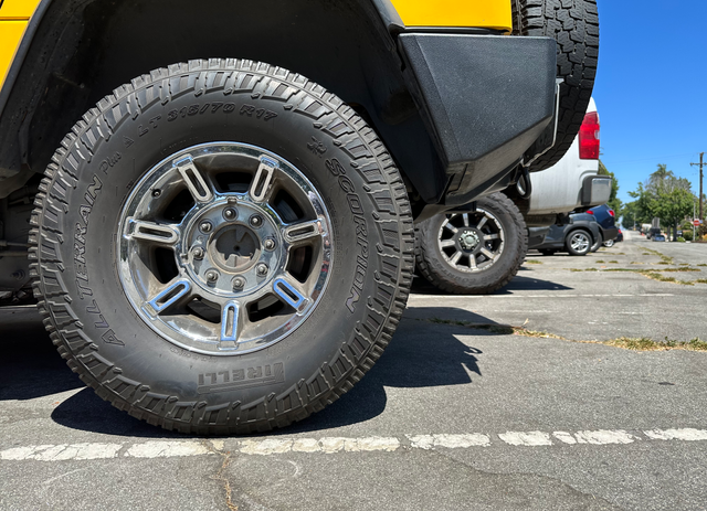 Large tires from several parked vehicles sit on a road with severe cracks and damage.