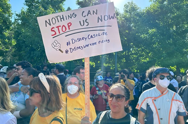 A crowd of people with a woman wearing sunglasses holding a sign that says "nothing can stop us now" in capital letters.