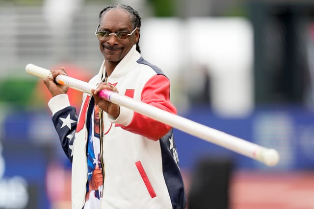 A man in glasses and a red, white and blue jacket holds a long pole