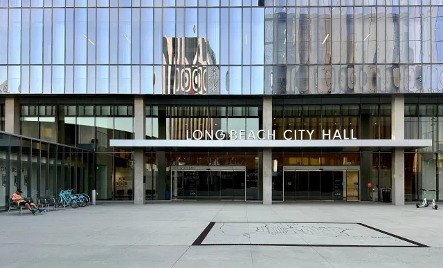 Downtown buildings reflected in the glass windows of another building labeled "Long Beach City Hall."