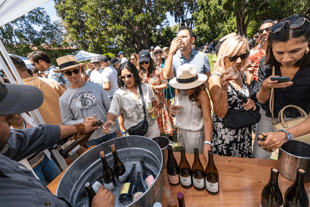 People stand around a metal tub holding seven bottles of wine.