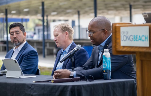 Three men in blue suits but without ties look bored while sitting at a table.