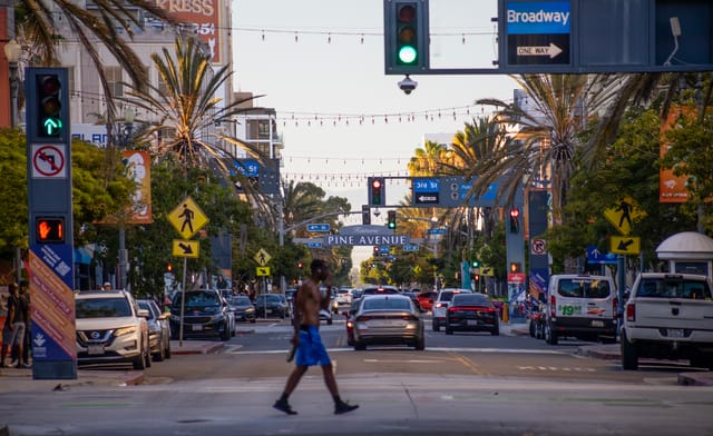 A man in blue shorts and no shirt crosses a busy city street.