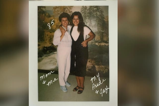 Two women stand next to each other in front of a large picture of a forest.