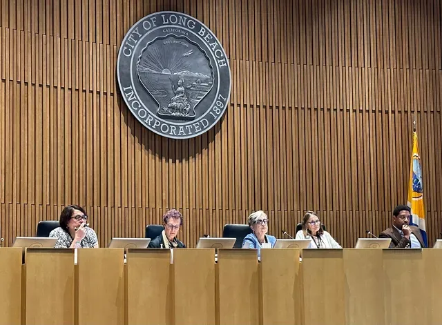 Five people look really bored while sitting on a beige dais in front of the seal of the City of Long Beach.