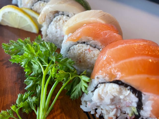 Sliced sushi rolls on a wood board next to a sprig of parsley.