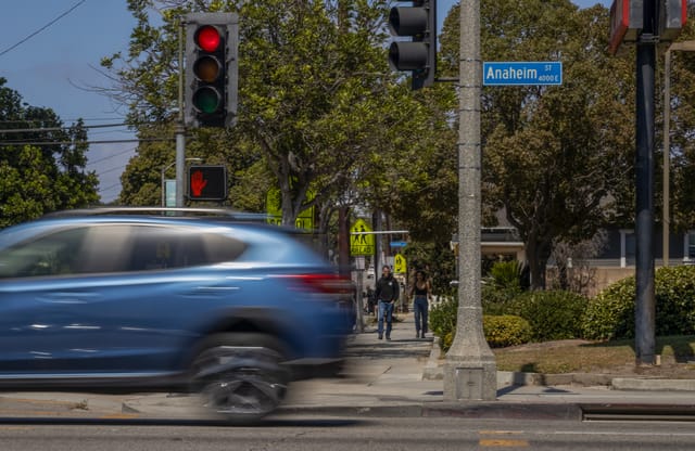 A blue car drives by in a blur as two people walk toward the camera.