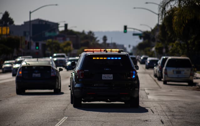 A police car drives away from the camera with lights on.