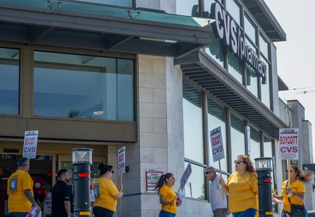 People wearing yellow shirts and signs that read "boycott CVS" stand in front of a CVS Pharmacy store.