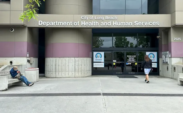 A woman walks into a building marked "City of Long Beach Department of Health and Human Services."