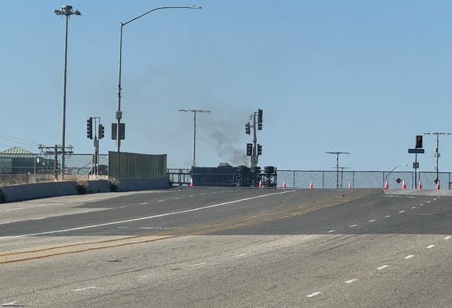 A trailer lays on its side on a road with black smoke rising.