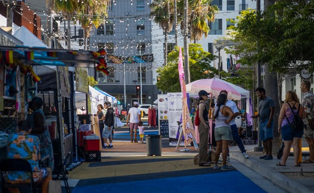 People stand near and walk by popup booths and tents selling food and other goods.