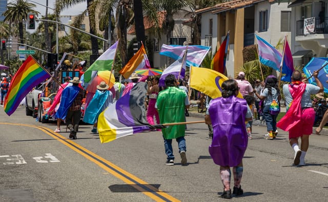 People wave brightly colored flags while walking down a street.