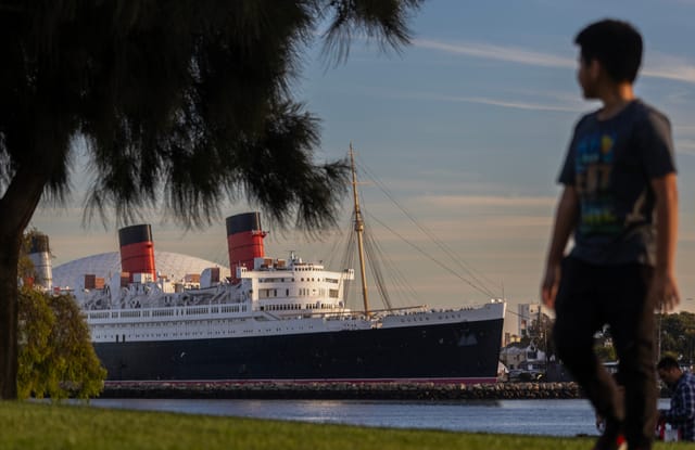 A child stands in front of a large black and white ocean liner.