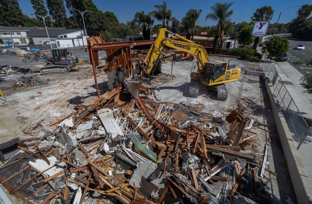 Debris from a demolished building surrounds a large, yellow piece of construction equipment.