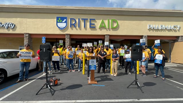 A large group of people wearing bright yellow shirts stand in front of building with signage that reads "Rite Aid."