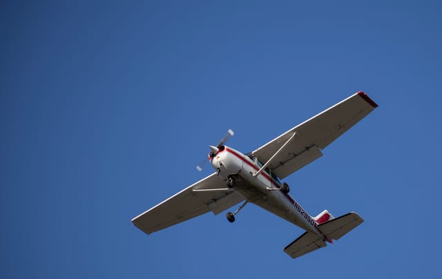 A small, white airplane flies through a clear blue sky.