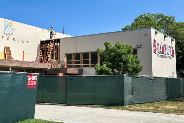 A construction workers stands on top of a building surrounded by a green fence.