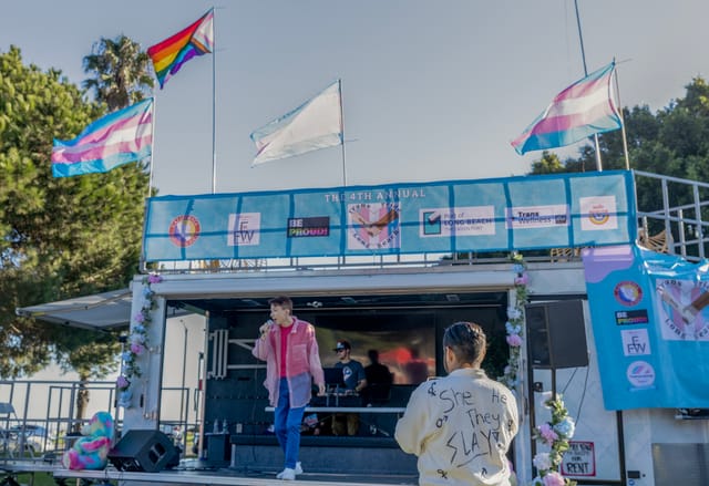 A person wearing jeans and a pink shirt sings on a small stage.