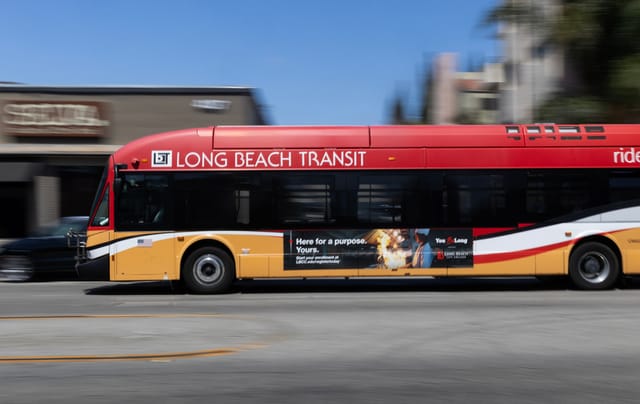 A red, yellow and white bus drives down a street with a blurred background.