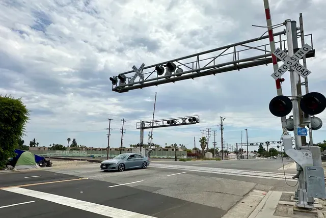 A gray car drives over railroad tracks at a road crossing.