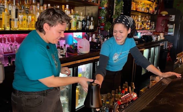 Two people smile as they work behind a cocktail lounge bar.