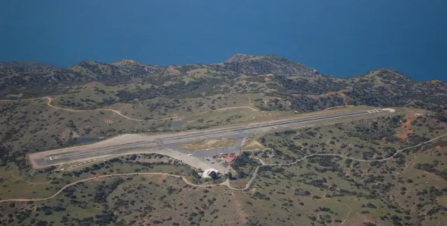 Aerial view of a very short airport runway in the hills near the ocean.