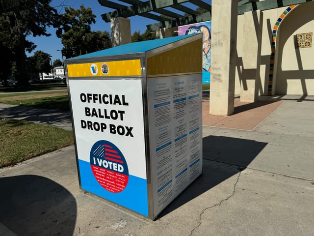 A white and yellow metal box label "official ballot drop box."