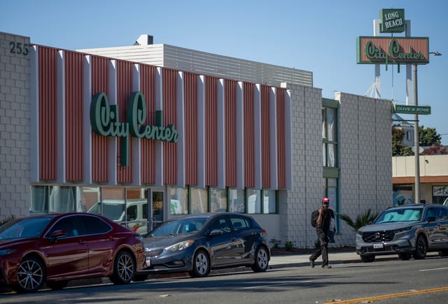 A person crosses the street away from a while and orange building that says "City Center" in green letters.