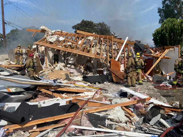 Firefighters move around among the rubble of a house that exploded.