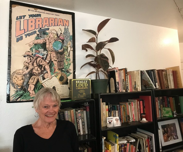 A person stands next to book shelves and a poster that says "Let your librarian be your guide."