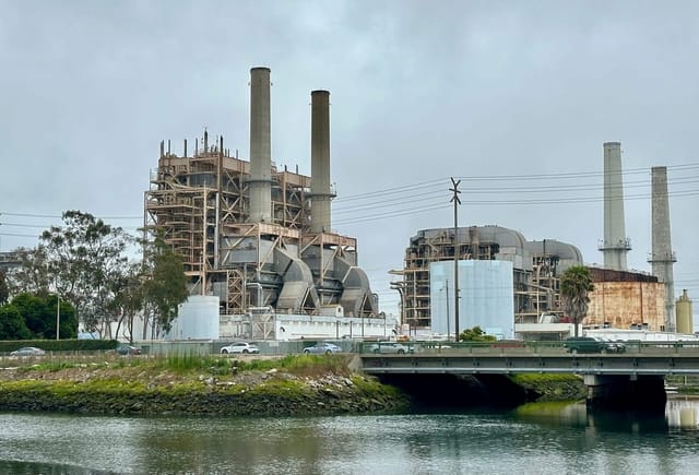 Gray power plant with four smokestacks situated near a river.