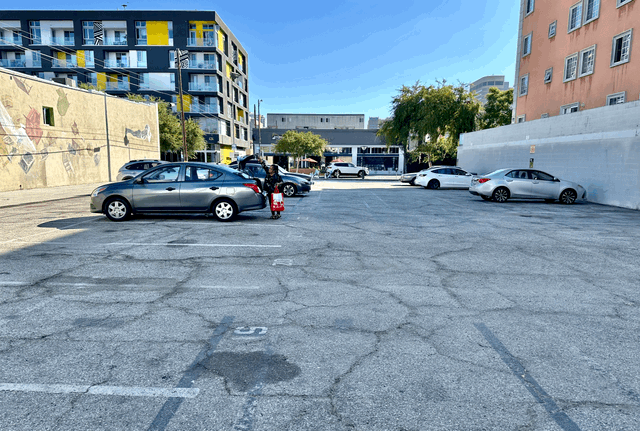 A person stands by a silver car in an old downtown parking lot.