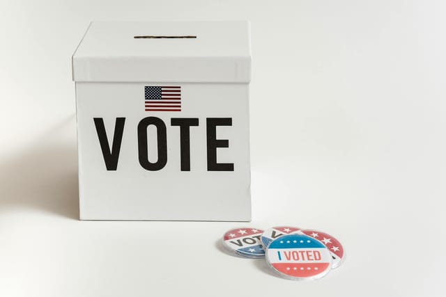 A white box with the word "VOTE" printed on it next to red, white and blue buttons saying "Vote" and "I Voted."