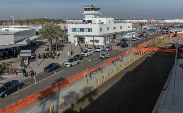 Travelers get out of cars and wait in lines at an airport near road construction.