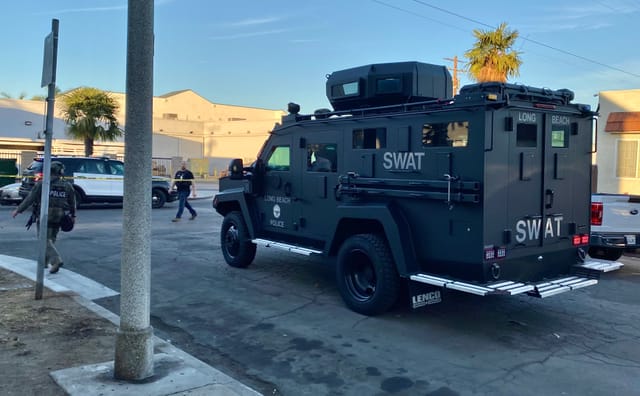 A black armored vehicle labeled SWAT drives slowly down a residential street.