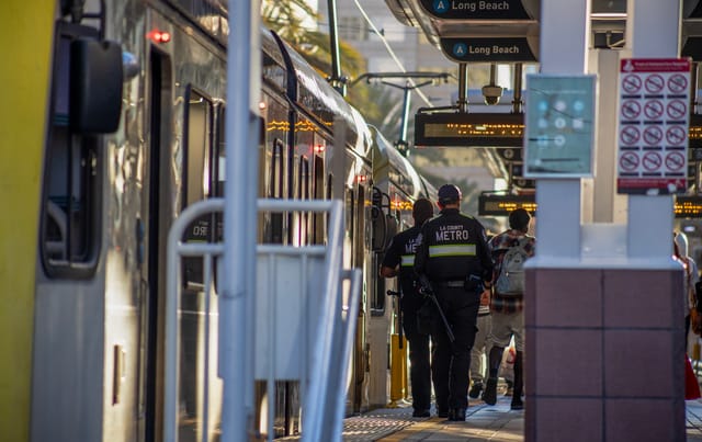 Two men wearing uniforms that say "LA County Metro" walk along a train platform.