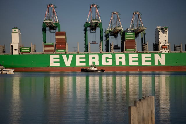 A green container ship with the word "evergreen" is unloaded by large cranes.