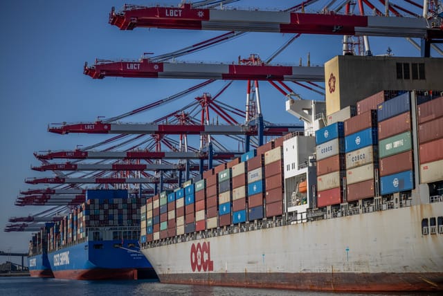 Three large ships hold thousands of shipping containers under massive red and white cranes.