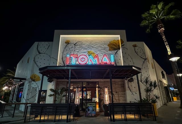 A restaurant with a blue and red neon sign that reads "Toma."