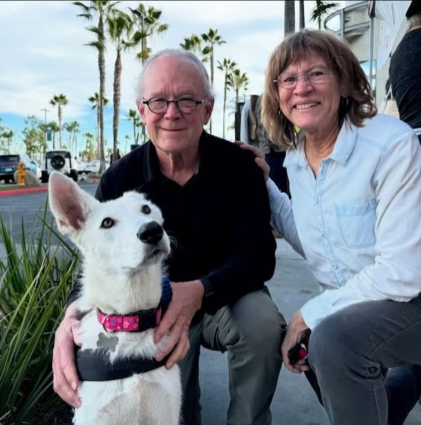 A man, woman and one-eared white dog pose on a street.