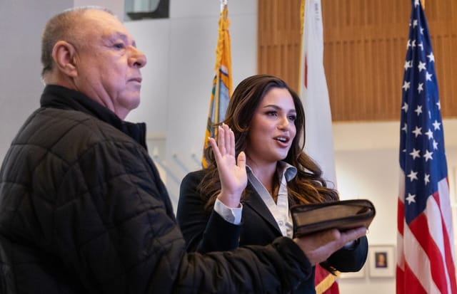 A young woman with long brown hair holds one hand on a bible held up by an older man.