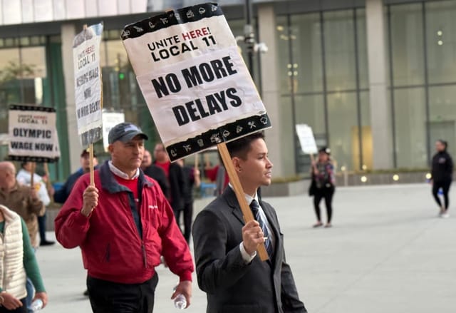 People carry signs that say "no more delays" and "Olympic wage now."