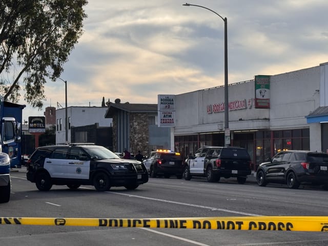 Police vehicles parked on a street behind yellow caution tape.