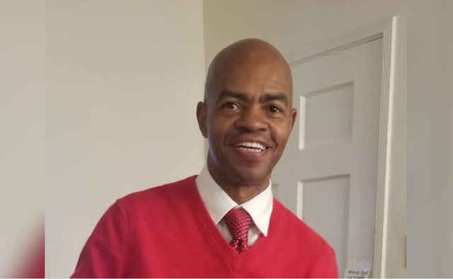 A bald man wearing a red sweater and red tie.